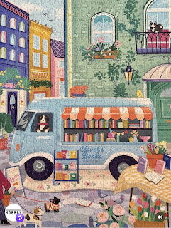 Illustrated book van on a pastel street with flowers, books, and cats outside tall buildings