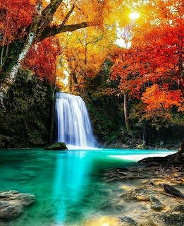 Waterfall cascading into turquoise pool surrounded by colorful autumn trees with red and orange leaves
