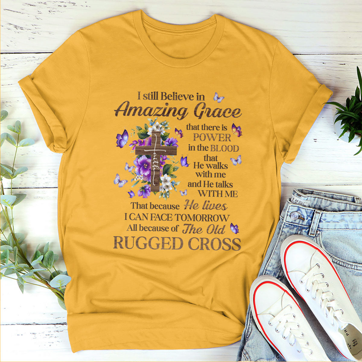 Yellow graphic T-shirt in a flat lay with white sneakers and small plants on a white wooden background