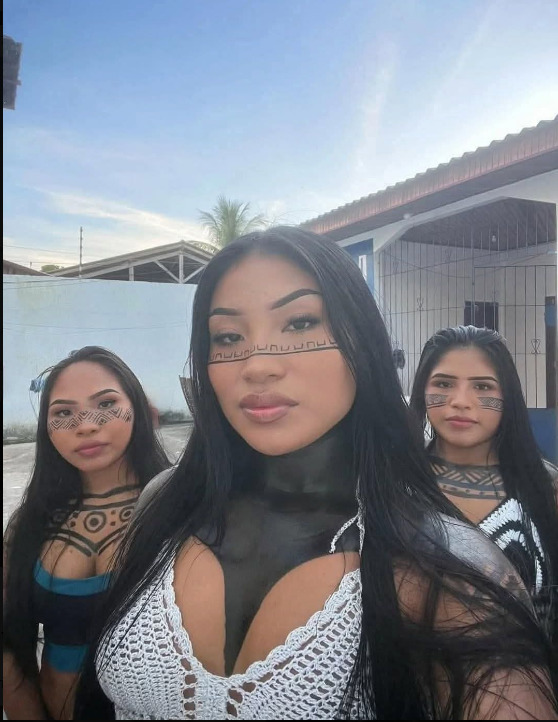 Three indigenous women with face and body paint taking a selfie outdoors