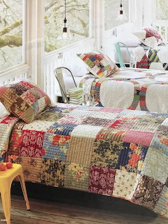 Daybed with colorful patchwork quilt in bright sunroom with white wicker furniture and large windows