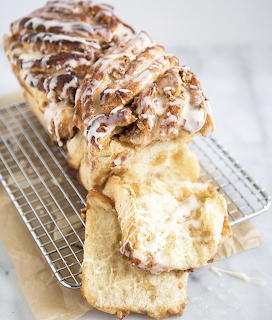 Sliced cinnamon swirl bread with white icing and almonds on cooling rack