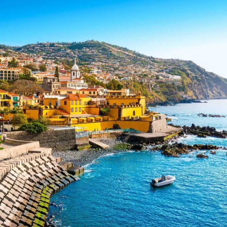 Coastal view of Funchal Portugal with colorful buildings on hillside, yellow fortress, and blue sea