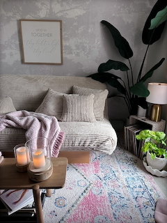 Cozy living room with cream sofa, candles, lamp, plants, and a pastel patterned rug