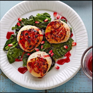 Three seared scallops on greens with pomegranate seeds and red sauce on a white plate