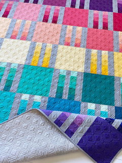 Colorful modern quilt with geometric picket fence pattern in pink, purple, teal, yellow blocks on white quilted backing