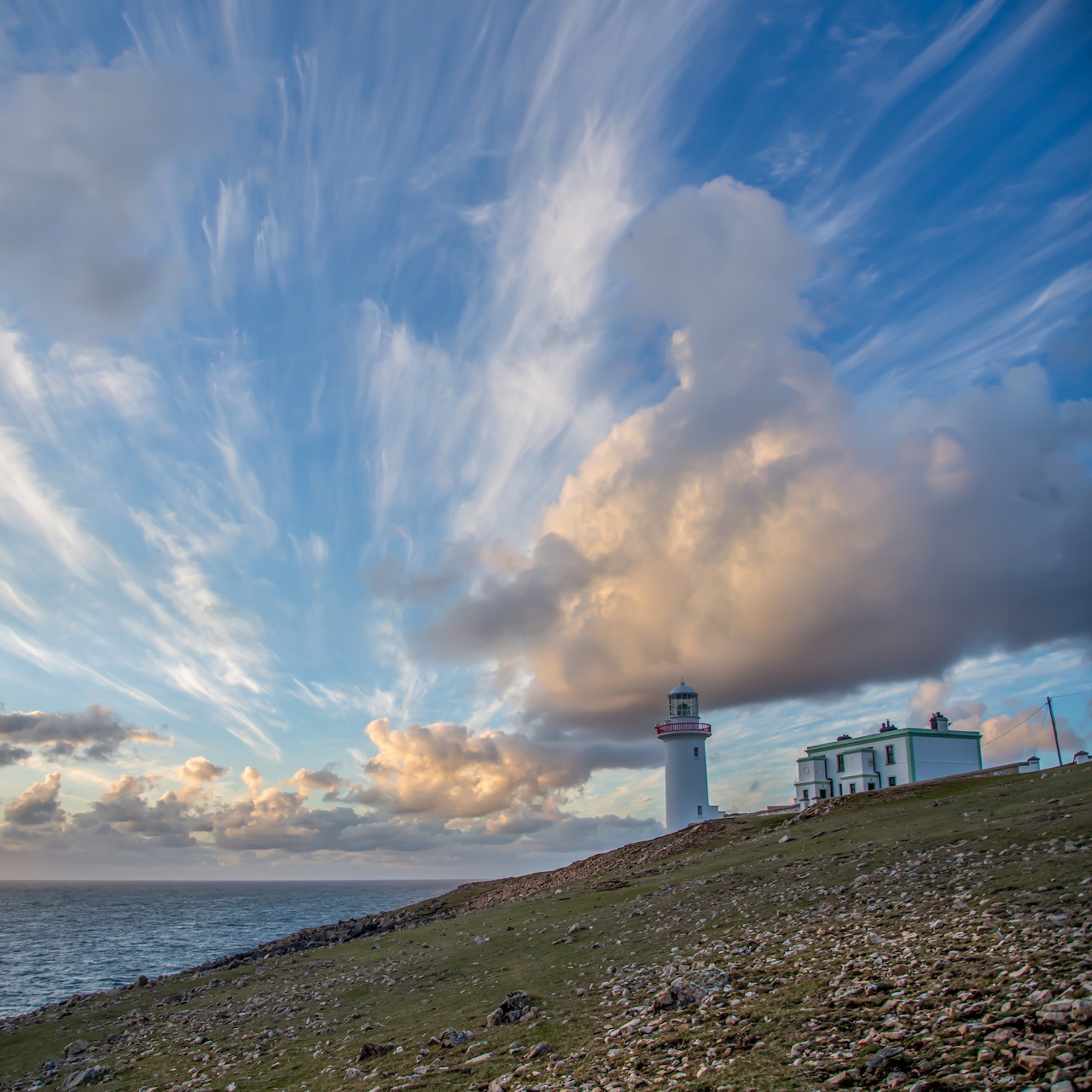 White lighthouse on a rocky coast under dramatic blue sky and towering clouds