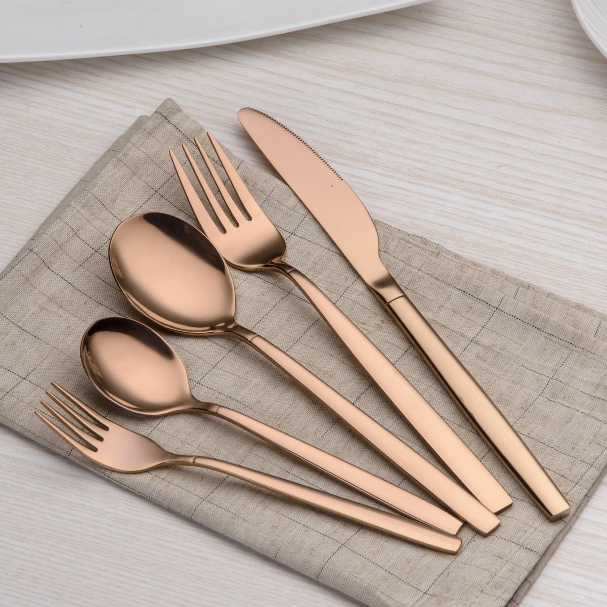 Rose gold cutlery set on a beige napkin over a light wooden table