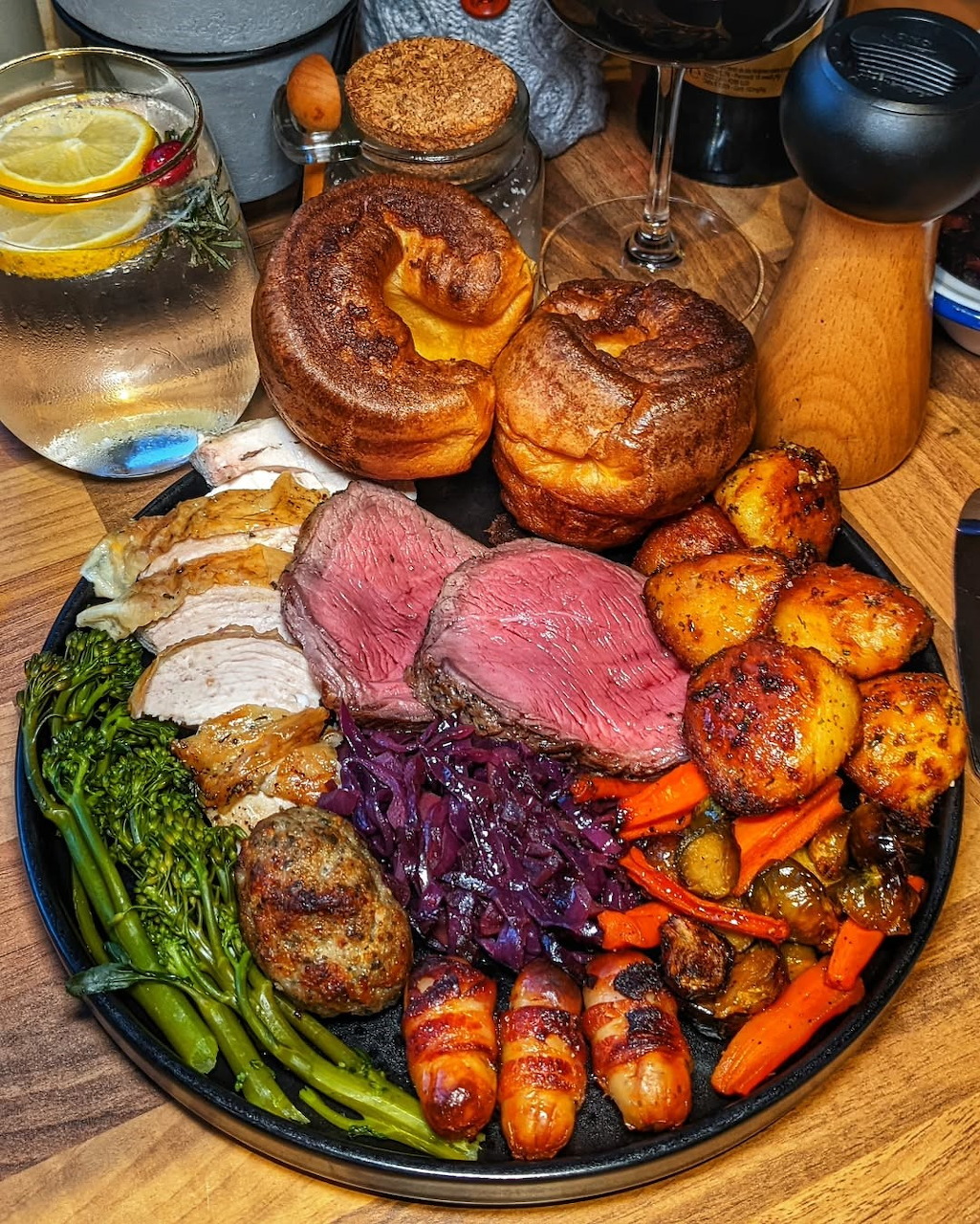 Overhead view of a full Sunday roast dinner with beef, Yorkshire puddings, vegetables, and gravy on a dark plate