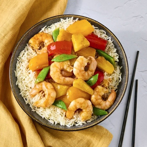 Bowl of sweet and sour shrimp with pineapple and vegetables over rice with chopsticks on the side