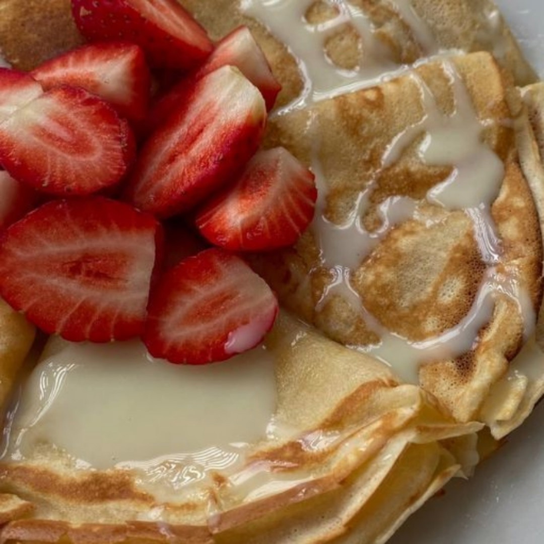 Folded crepes topped with sliced strawberries and drizzled with condensed milk on a plate