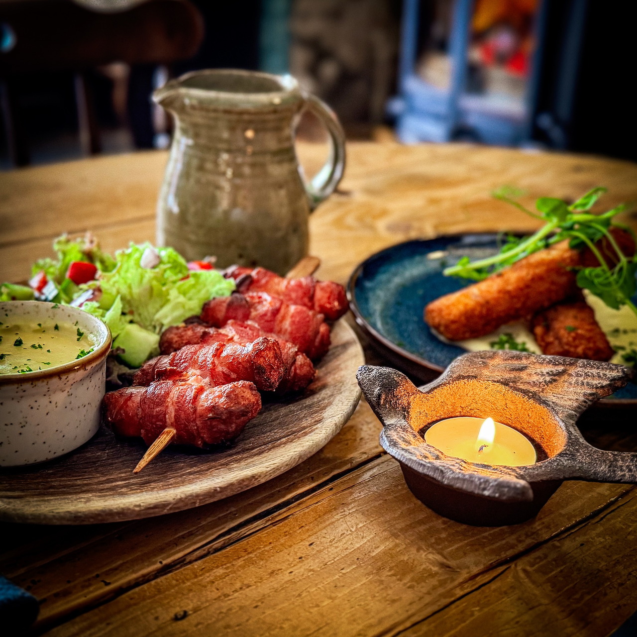 Wooden platter with red meat skewers, sauces, fried spring rolls, and garnish on restaurant table
