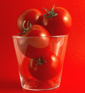 Three ripe red tomatoes with stems in a clear glass on red background