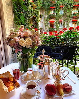 Breakfast table with bouquet and pastries on balcony overlooking ivy-covered building with red flowers