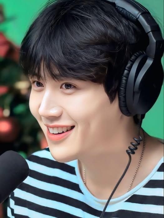 Young Asian man smiling with black headphones and striped shirt near a microphone