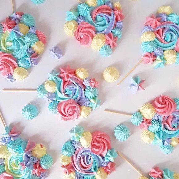 Pastel-colored meringue lollipops with rosette and flower decorations on sticks against a white background