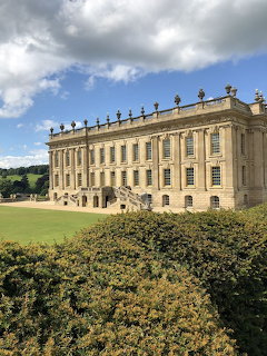 Stately Chatsworth House with formal gardens under cloudy blue sky