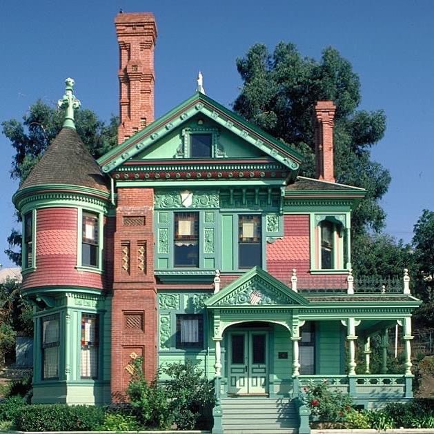 Victorian house with green siding, ornate trim, red brick chimneys, and turret