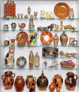 Glass shelves filled with vintage pottery, ceramic jugs, figurines, plates, and antique collectables
