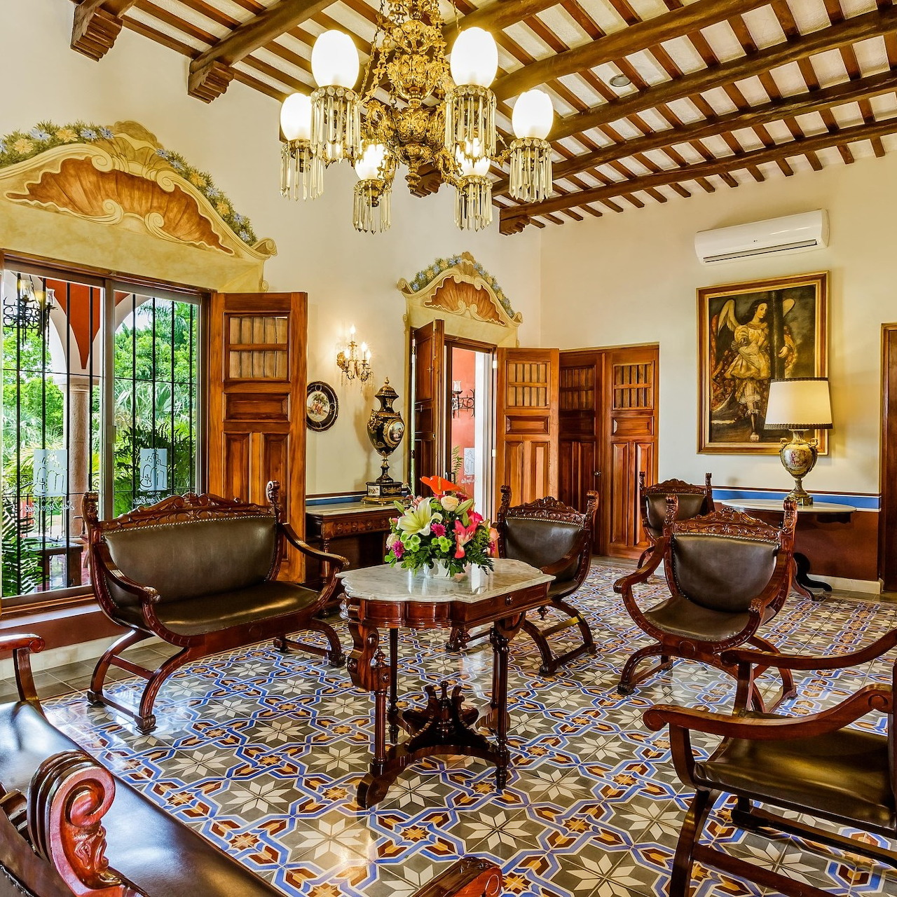 Elegant historic sitting room with carved wood chairs, patterned tile floor, chandeliers, and shuttered windows
