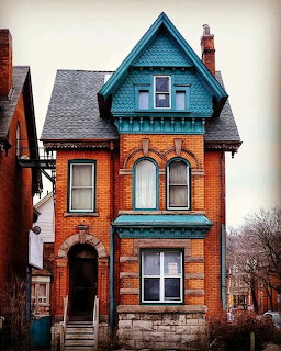Narrow Victorian brick house with teal trim, arched windows, and a steep gabled roof