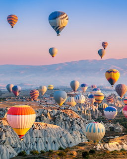 Colorful hot air balloons drifting over Cappadocia's rocky landscape at sunrise