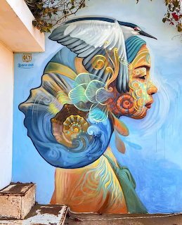 Colorful street art mural of a face with abstract ocean-themed patterns on blue wall