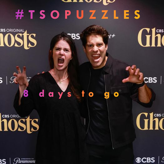 Two people posing playfully at a Ghosts TV show premiere event backdrop