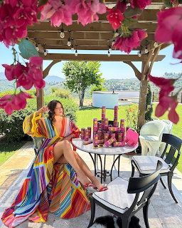 Woman in vibrant striped dress sitting at patio table under flower-covered pergola with lake view