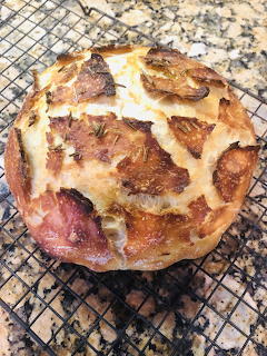 Round rustic no-knead bread loaf on a wire cooling rack over a speckled countertop