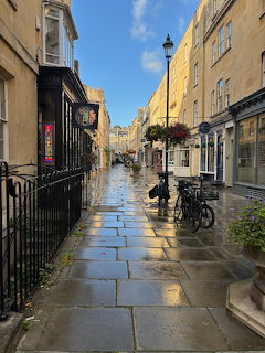 Narrow wet city street with historic buildings, bicycles, and hanging flower baskets