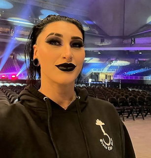 Drag performer with dramatic makeup in black hoodie at concert venue with purple stage lights