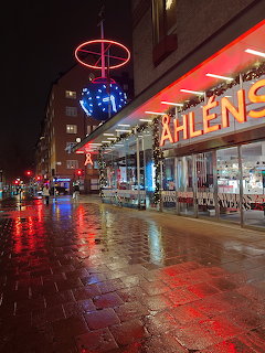 Åhlens department store facade lit with red neon signs at night on a wet Stockholm street