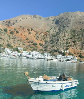 White fishing boat in calm bay at Loutro village, Crete, with mountains and white buildings in background