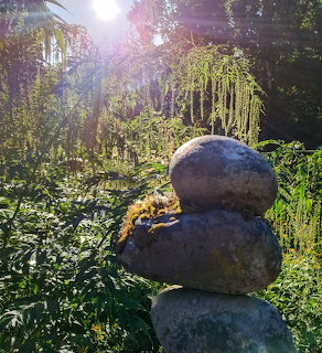Three stacked stones balanced in sunlit garden with purple wisteria flowers