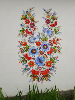 Colorful folk art mural of flowers and blue birds on a white wall above grass