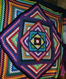 Colorful crocheted mandala blanket with rainbow geometric patterns and hexagonal center in granny square style