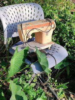 Vintage sewing machine on a gray chair among green plants outdoors