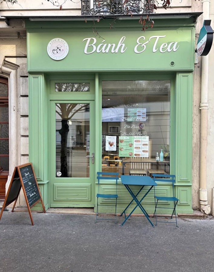 Mint green shopfront with glass door, window, chalkboard sign, and a small table with two chairs