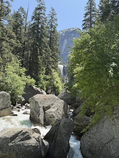 Rocky stream with boulders and pine trees leading to a distant waterfall in Yosemite