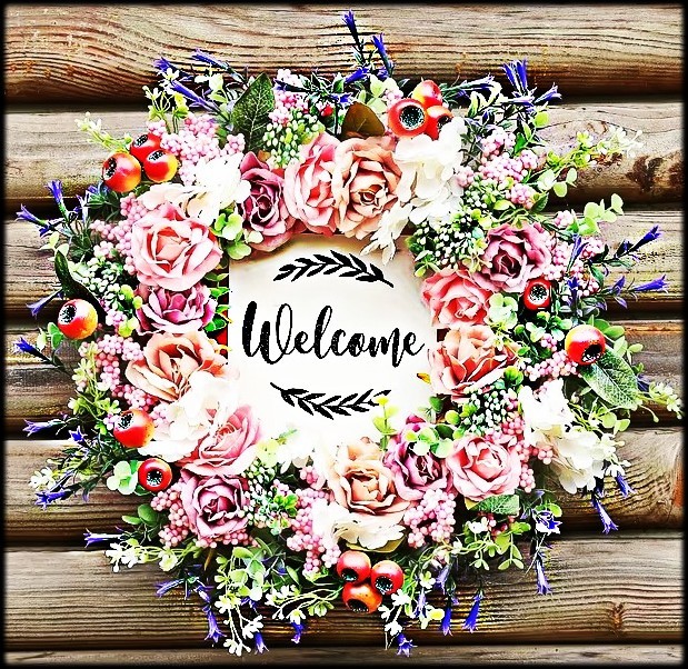 Floral wreath with pink roses and berries around a welcome sign on rustic wood