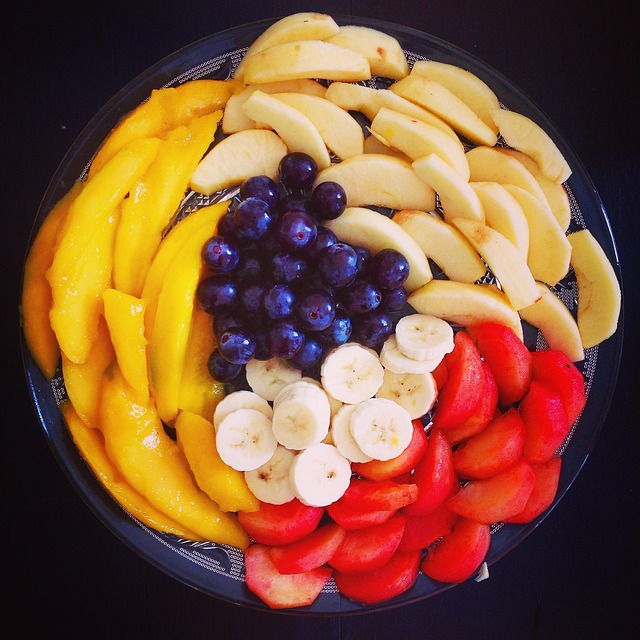 Round fruit platter with mango, pear, strawberries, banana slices, and purple grapes