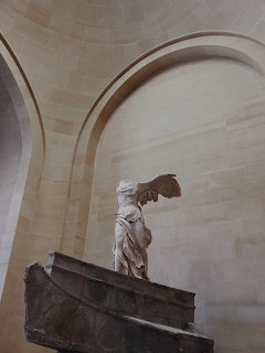 Winged Victory of Samothrace statue in a stone arched niche with soft lighting
