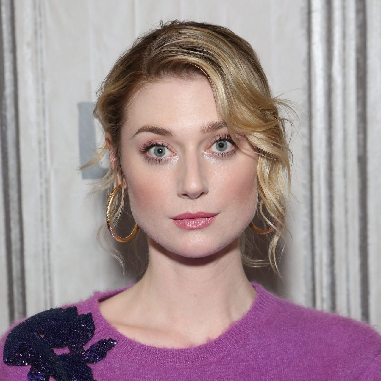 Portrait of blonde woman in purple top with gold earrings