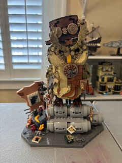 Intricate steampunk owl LEGO build with gears, clocks, and brass details on a gray display base
