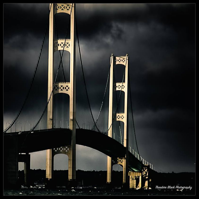 Suspension bridge with lit towers under dark stormy sky