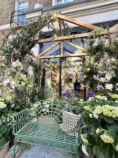 Flower-covered Chelsea entrance with a green bench and abundant white, purple, and green blooms
