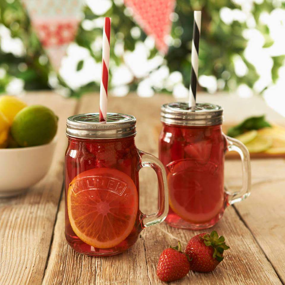 Two mason jars with strawberry lemonade, orange slices, and striped straws on wooden table with fresh strawberries
