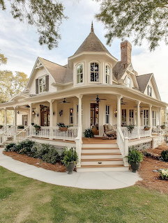 Cream Victorian farmhouse with turret and wraparound porch surrounded by lawn and trees