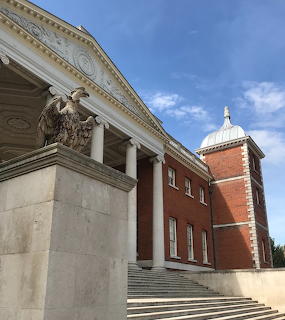 Neoclassical facade of Osterley House with stone columns, eagle sculpture, red brick, and domed cupola against blue sky